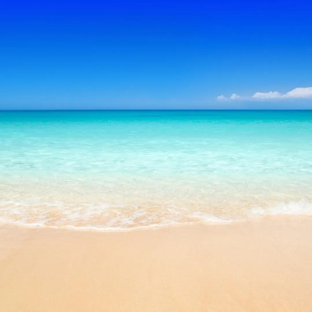 Turquoise ocean waves gently washing onto a soft white-sand beach under a clear blue sky.